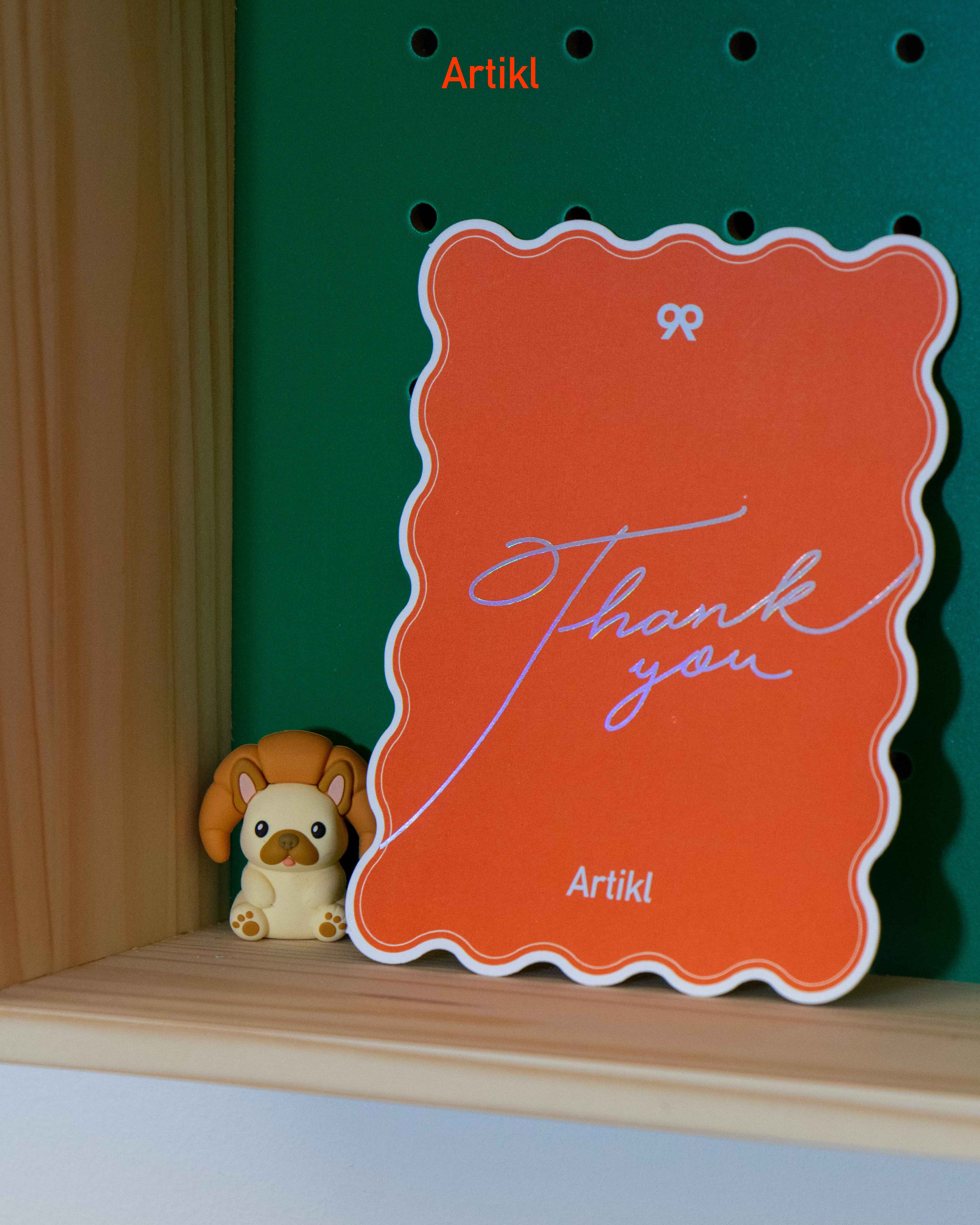Peek-a-Pals puppy collectible figure displayed beside Artikl thank you card on wooden shelf as a cute desk companion