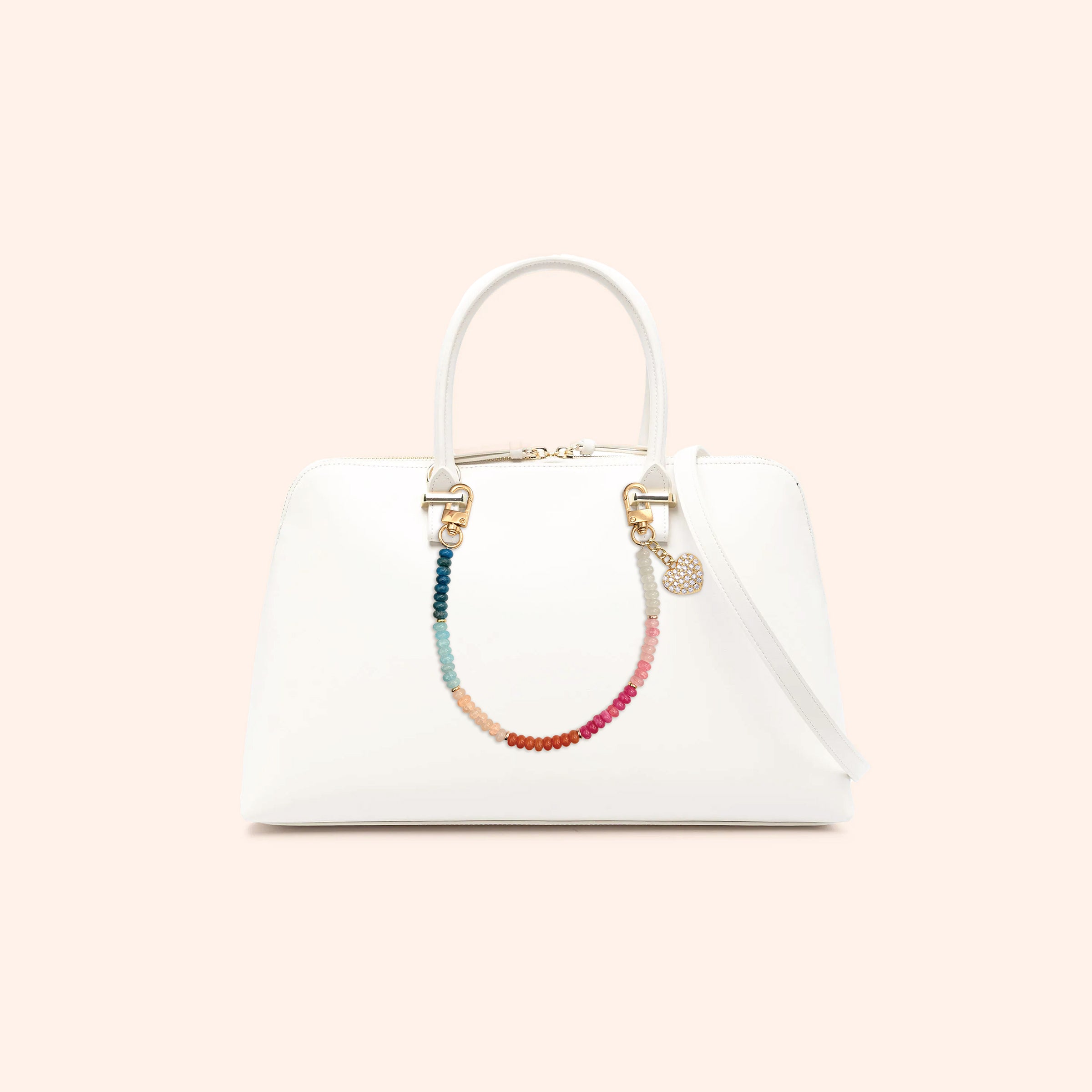 White handbag with a Rainbow Beaded Heart Phone Charm on a light pink background