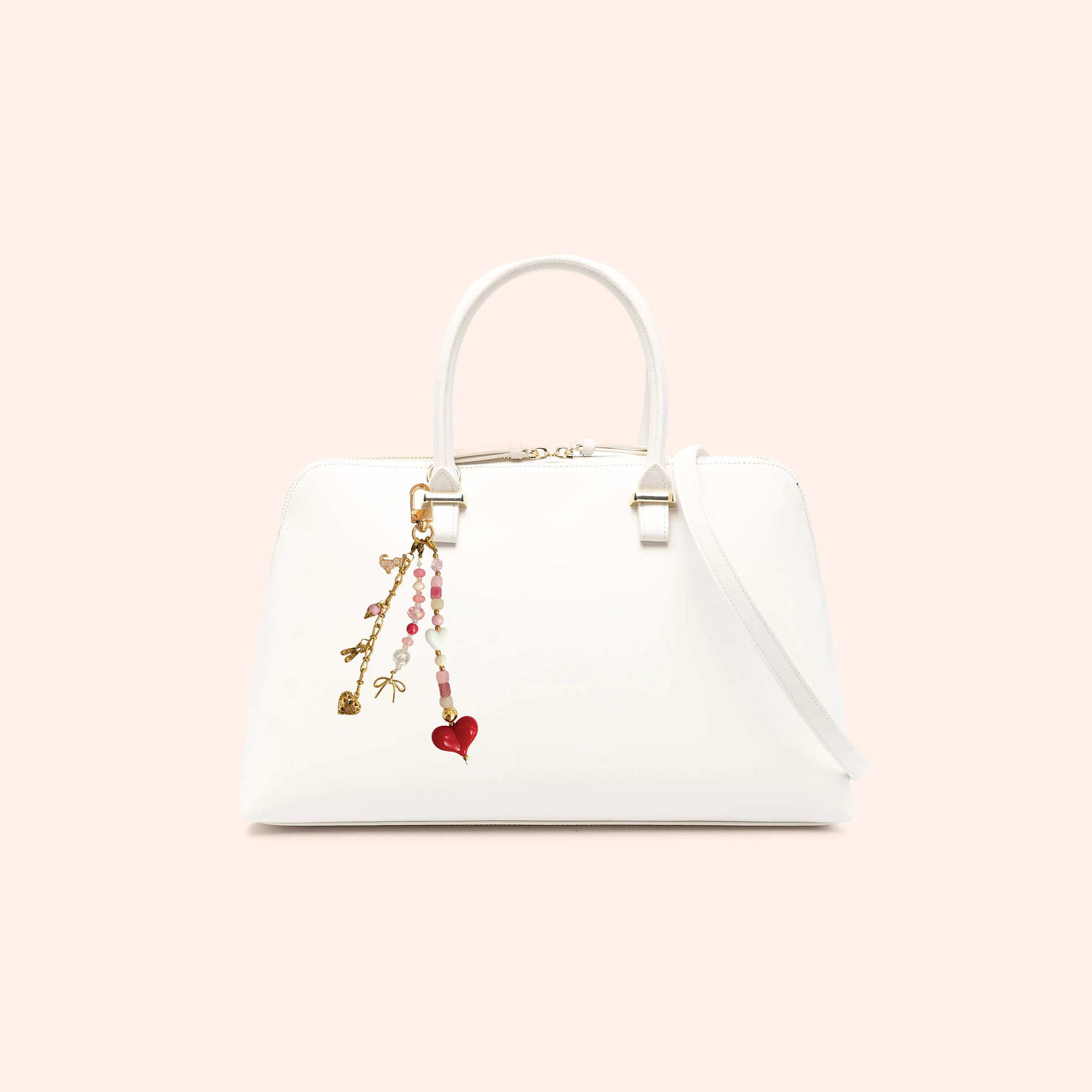 Heart-themed beaded bag charm attached to white handbag featuring pink gemstone beads, crystal accents, gold-tone details, and red heart pendant