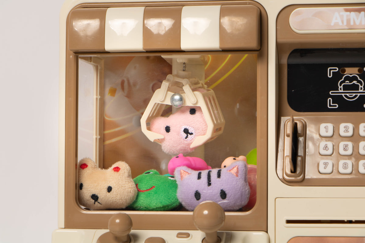 Artikl 2-in-1 Claw Machine & ATM Piggy Bank for Kids, close-up view showing the plush prizes inside the claw machine and the ATM screen