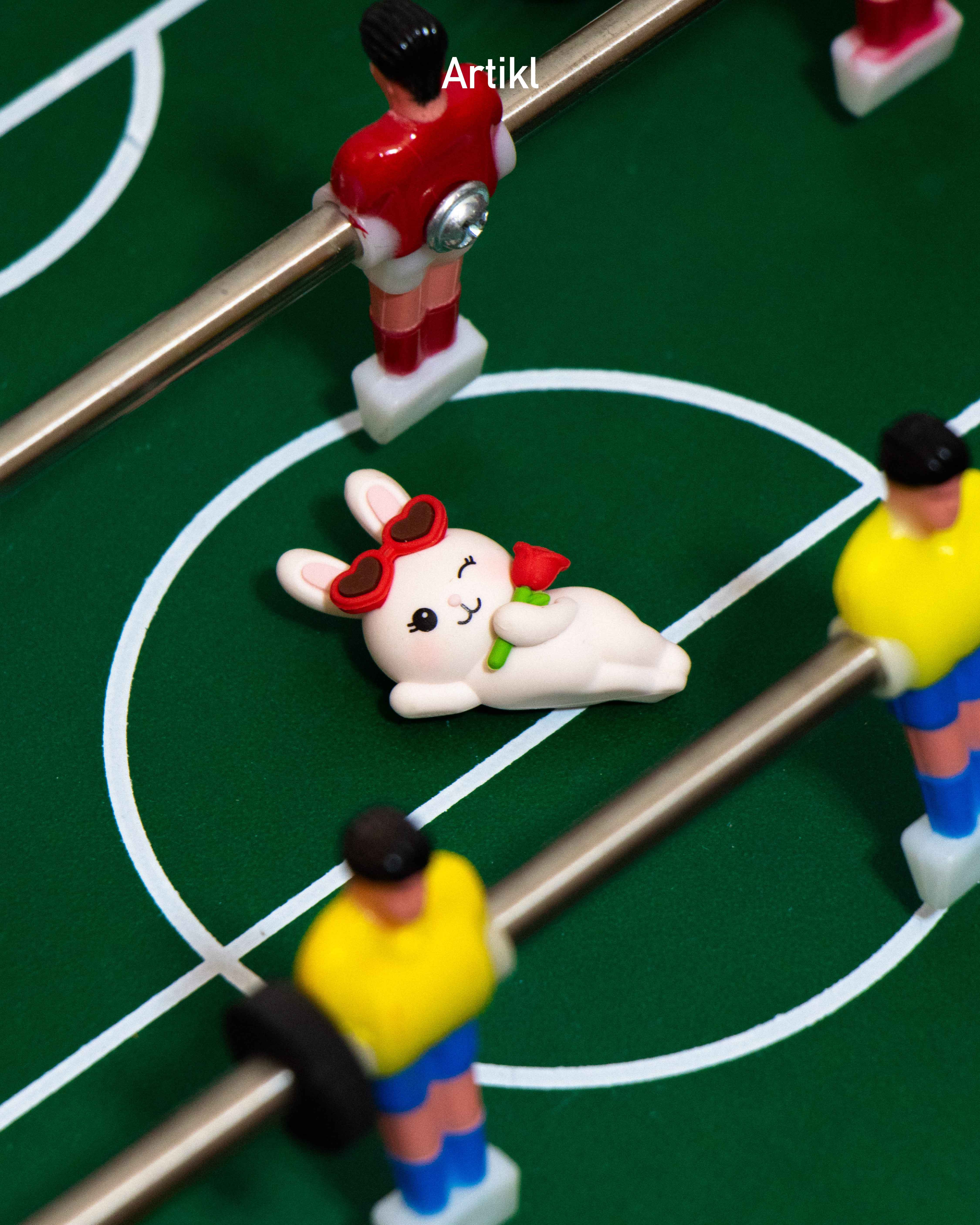 Peek-A-Pals Love Notes Bunny collectible figure featuring heart-shaped sunglasses and a red rose, displayed as a playful desk decoration on a foosball table