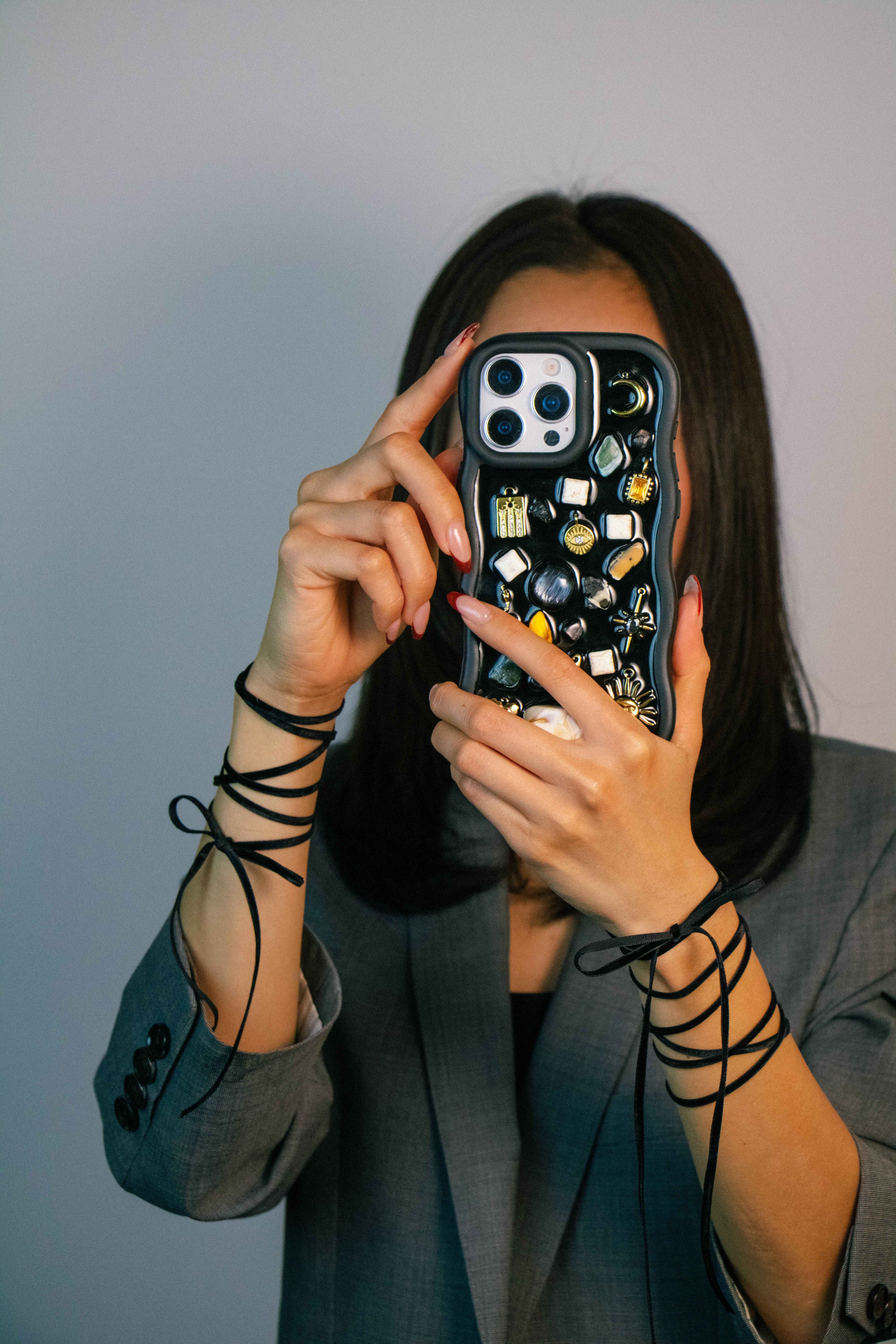 Model using a Black Mosaic handcrafted charm phone case featuring celestial charms, gemstone-inspired details, and a unique statement design