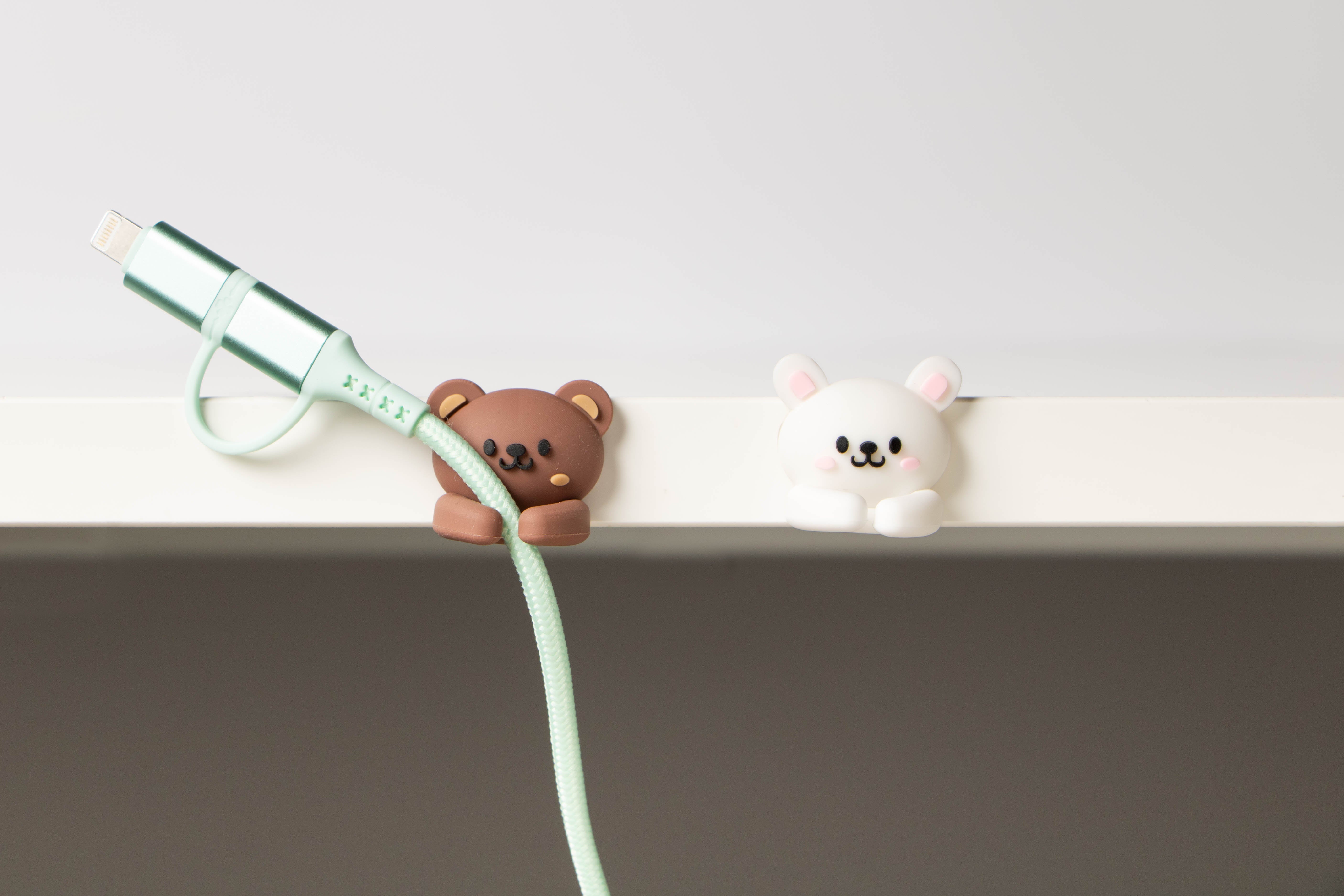 Bunny & Bear Cable Clip Organizer attached to a desk edge holding a mint green charging cable, highlighting everyday desk cable management