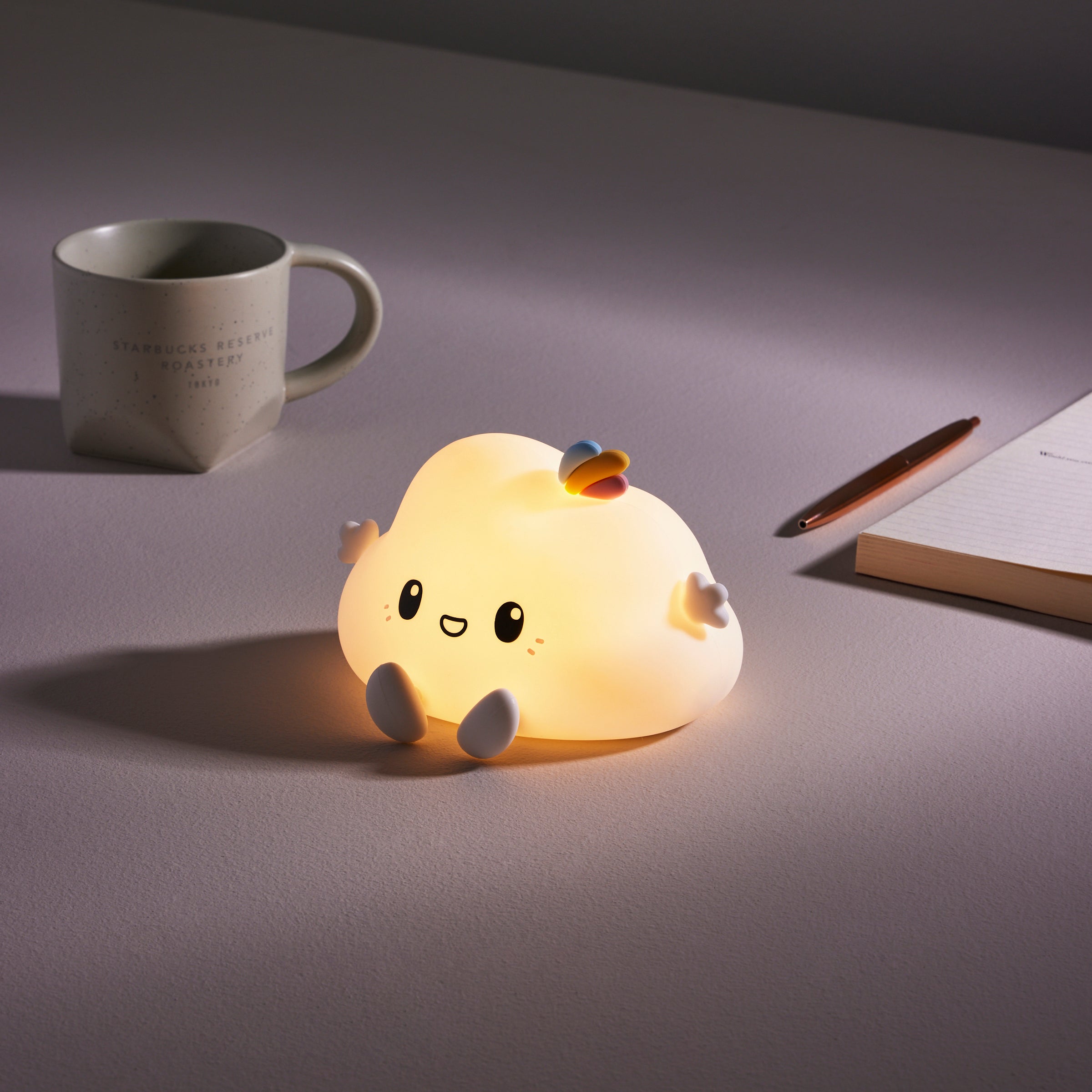 Cute silicone cloud night light glowing on desk with rainbow detail