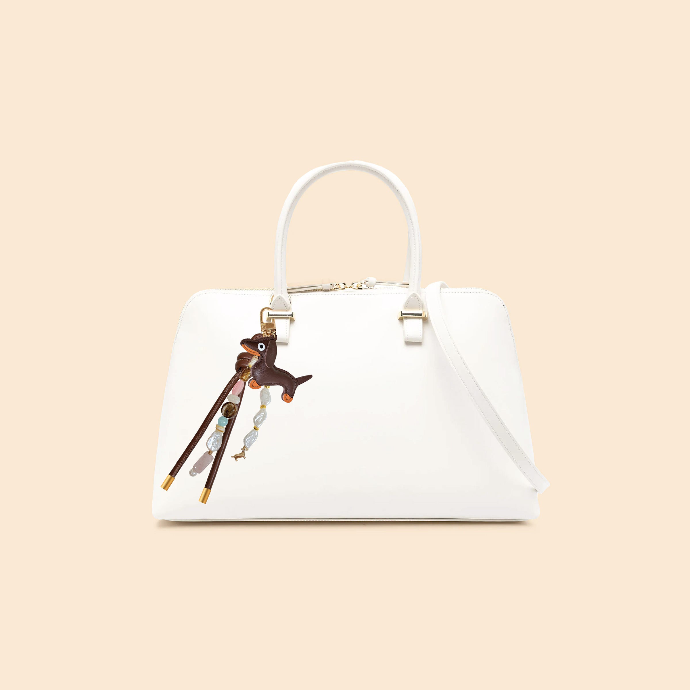 Dachshund-inspired bag charm attached to white handbag featuring leather dog pendant, gemstone-style beads, pearl accents, decorative tassels, and gold-tone hardware
