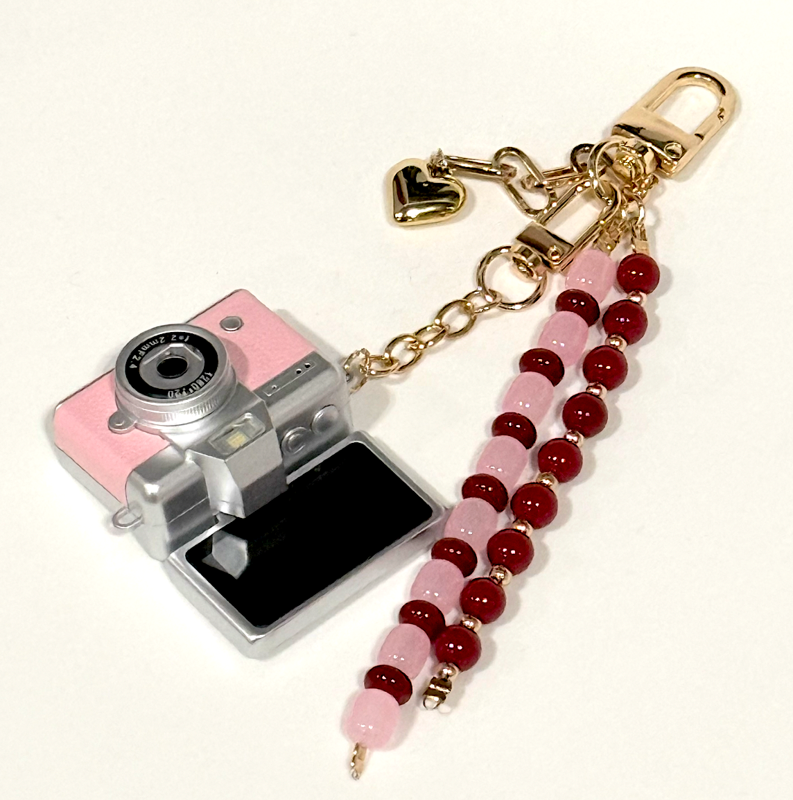 Artikl Mini Retro Keychain Digital Camera Charm in Blush Pink styled on a neutral fabric surface, highlighting the beaded tassel and heart charm