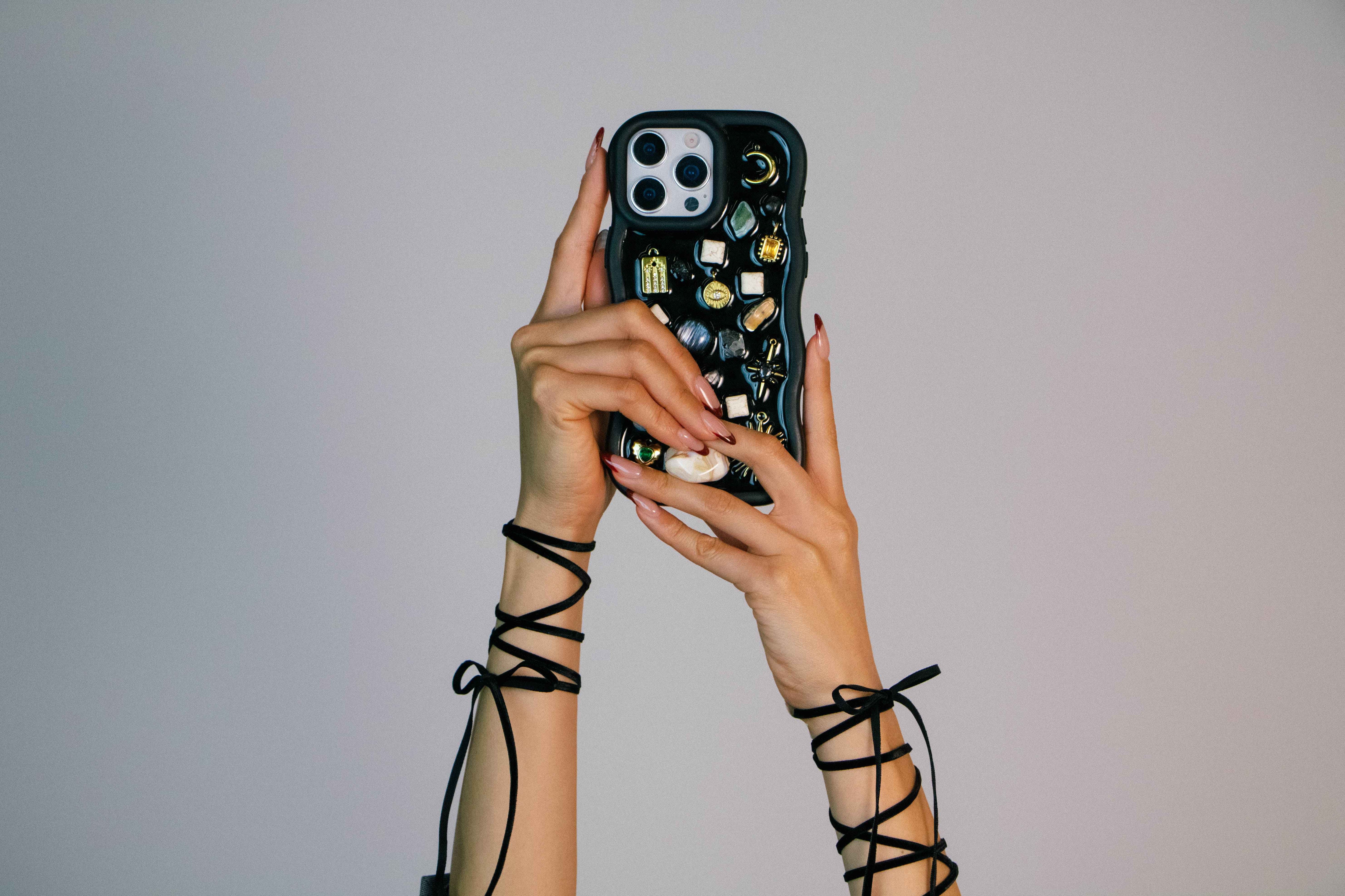 Black Mosaic charm phone case held in hand, featuring handcrafted decorative charms, celestial details, and a unique statement design for iPhone users